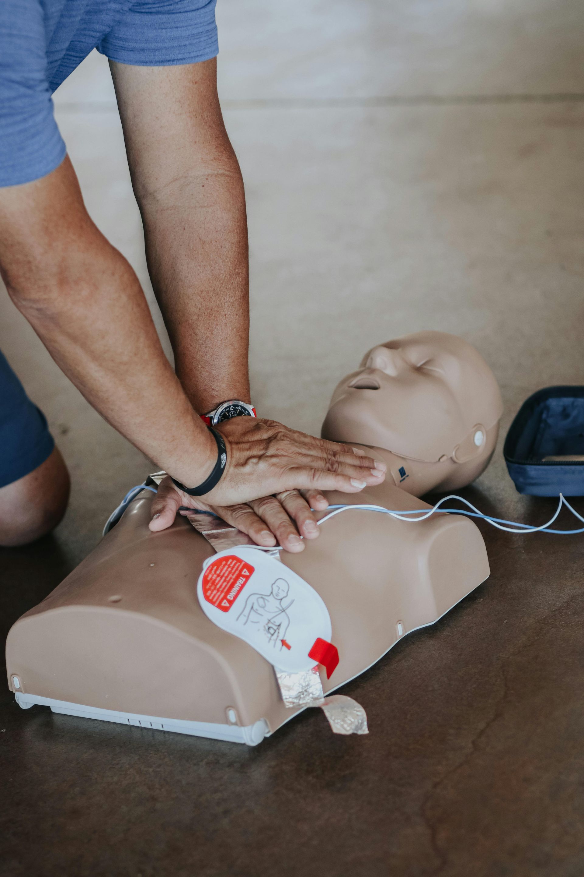 Hands performing CPR chest compressions on a CPR training mannequin.