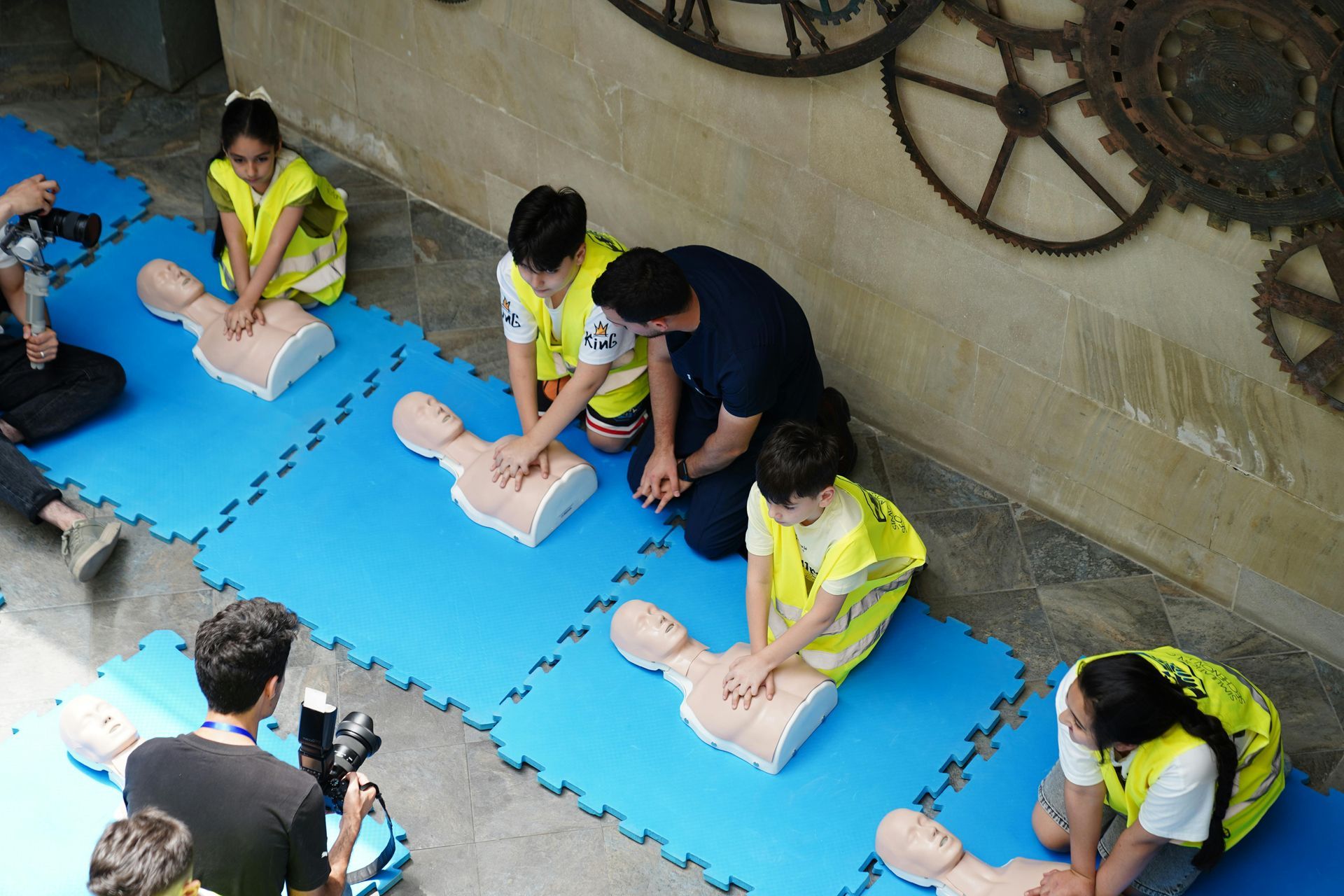 People practicing CPR on training mannequins on blue mats, with an instructor observing nearby.