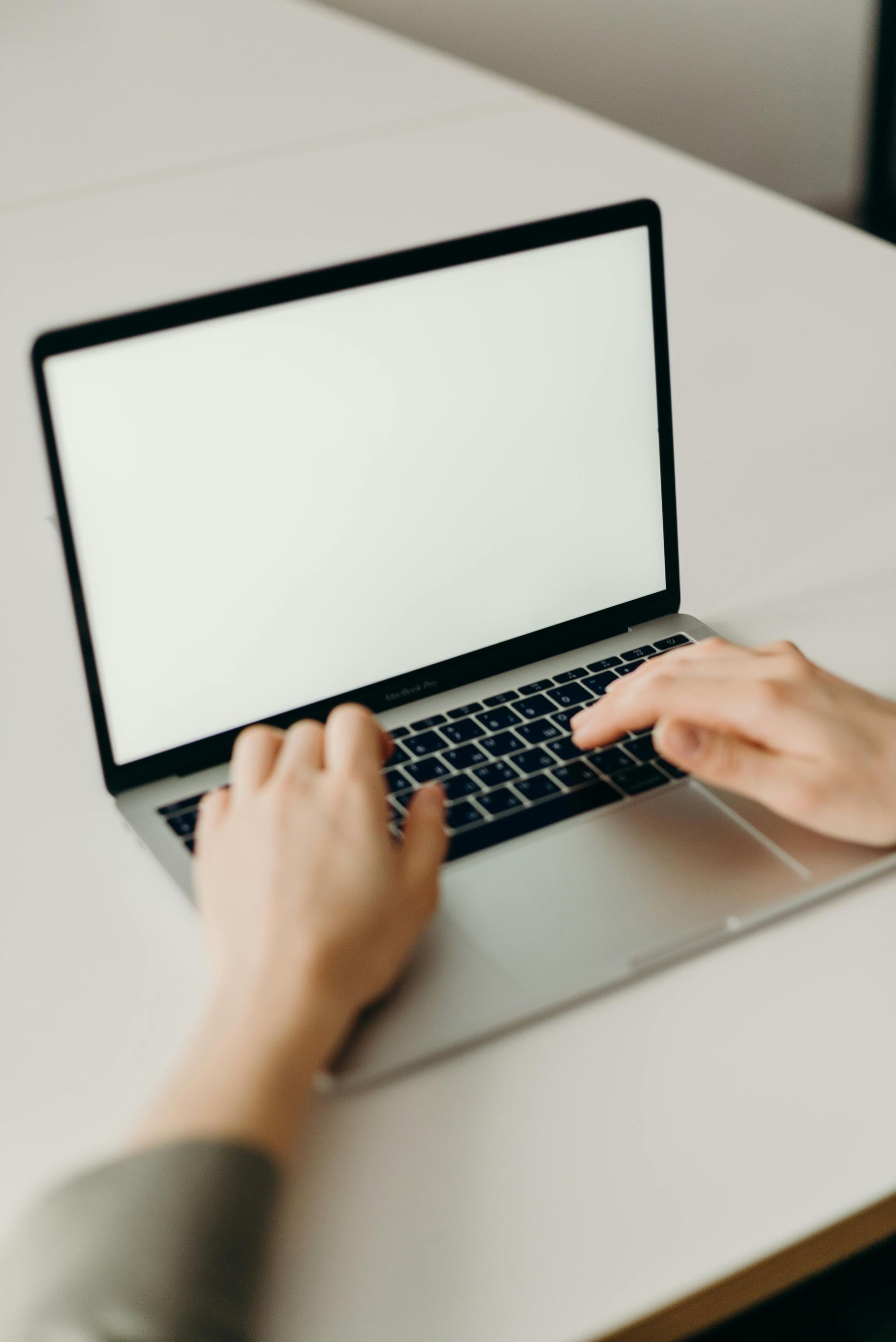 Hands typing on a laptop with a blank screen at a desk