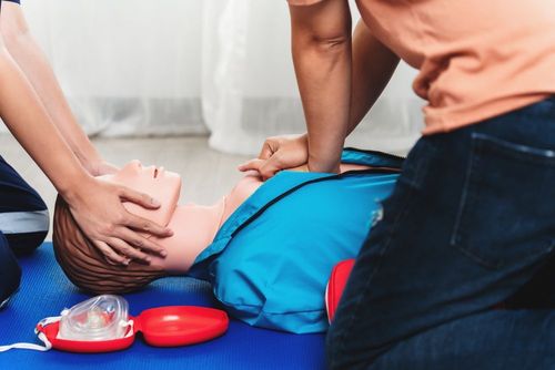 Two people perform CPR on a person lying on a blue mat with a rescue mask nearby