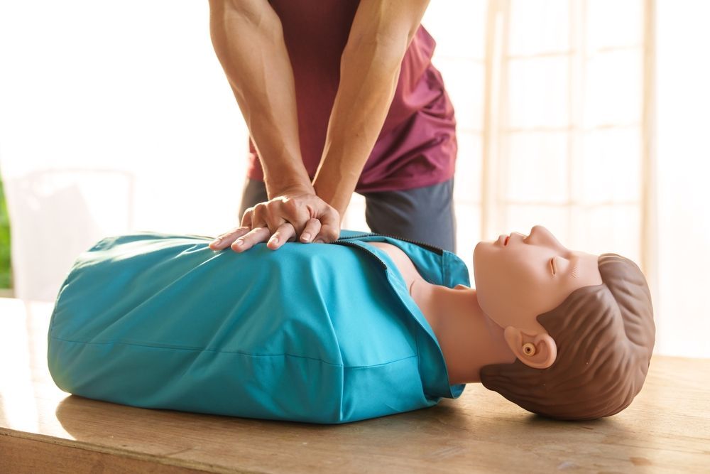 Person performing CPR chest compressions on a mannequin on a wooden floor
