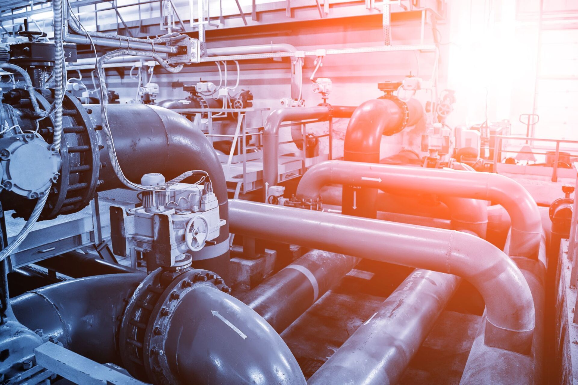 Sistema di tubazioni industriali in un ambiente di fabbrica con una luce intensa sulla destra.