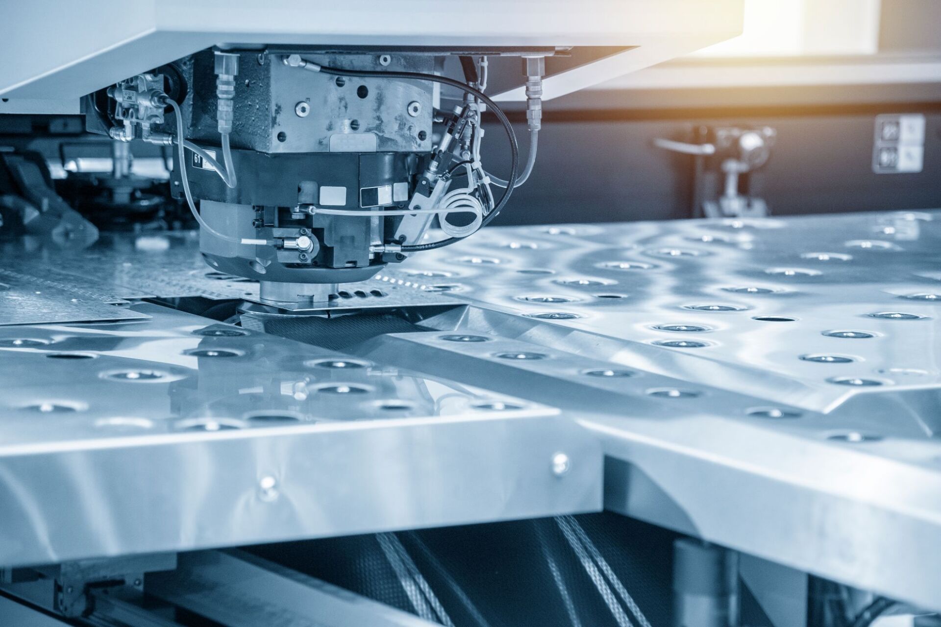 Primo piano di una macchina per lo stampaggio dei metalli che pratica un foro in una lamiera sul pavimento di una fabbrica industriale.