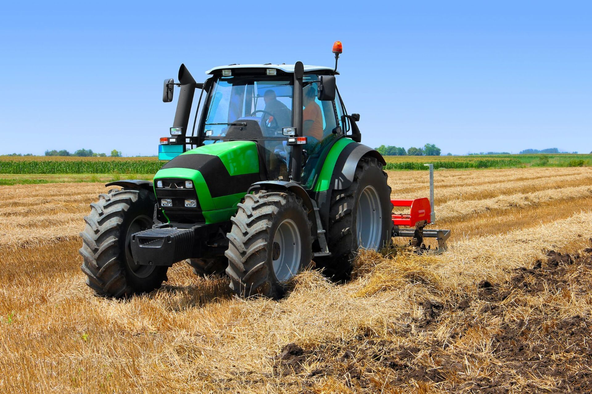 Un trattore verde ara un campo sotto un cielo azzurro e terso, evidenziando il contrasto tra la stoppia e il terreno scuro arato.