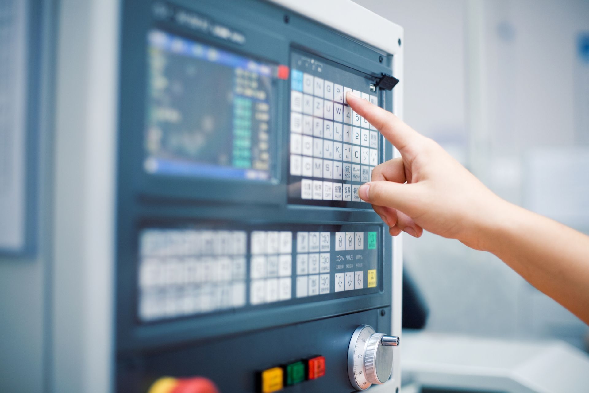 In un ambiente industriale, il dito di una persona preme un pulsante sul pannello di controllo di una macchina dotata di schermo digitale.