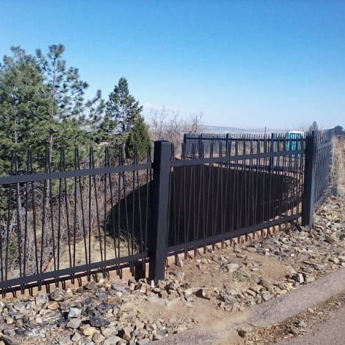 A black fence surrounds a rocky area with trees in the background