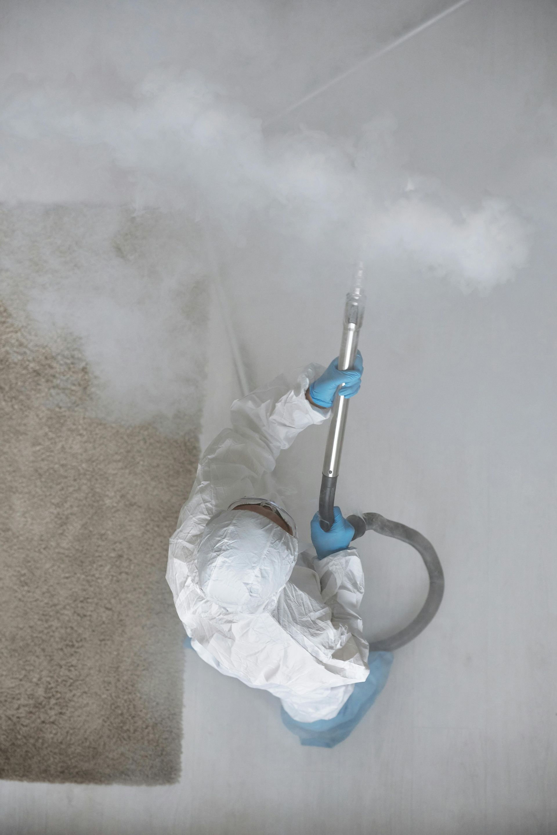 A person in a protective suit is using a vacuum cleaner to clean a wall.