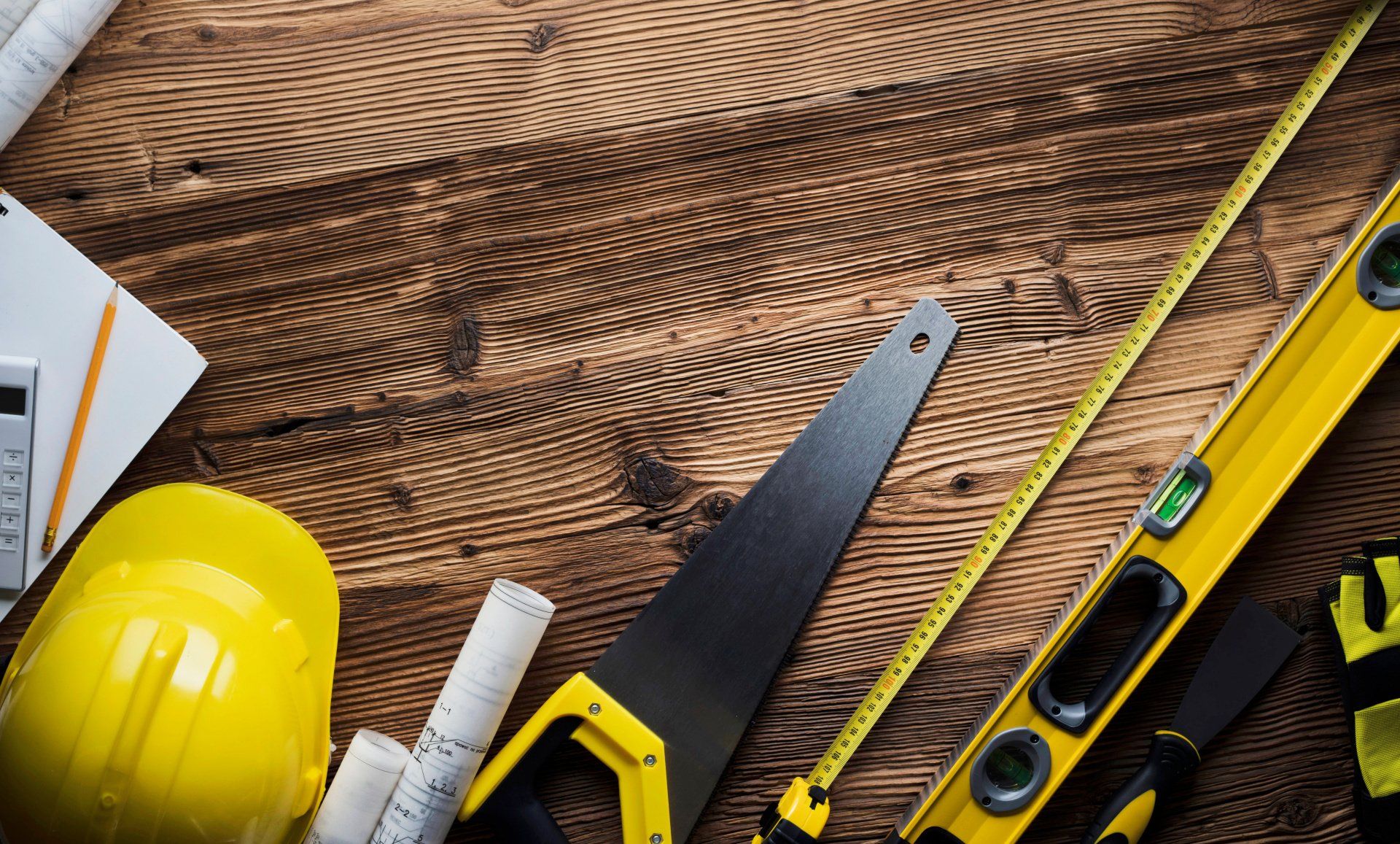 A wooden table topped with construction tools , a hard hat , a tape measure , and a saw.