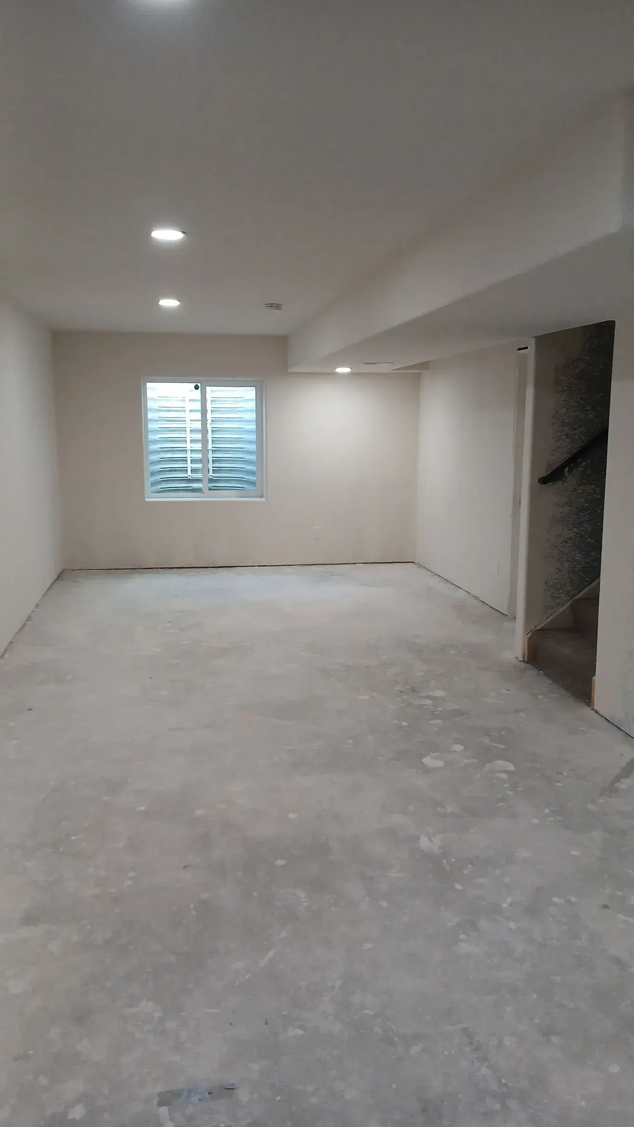 Empty interior room with concrete floor, small window, and recessed lighting.