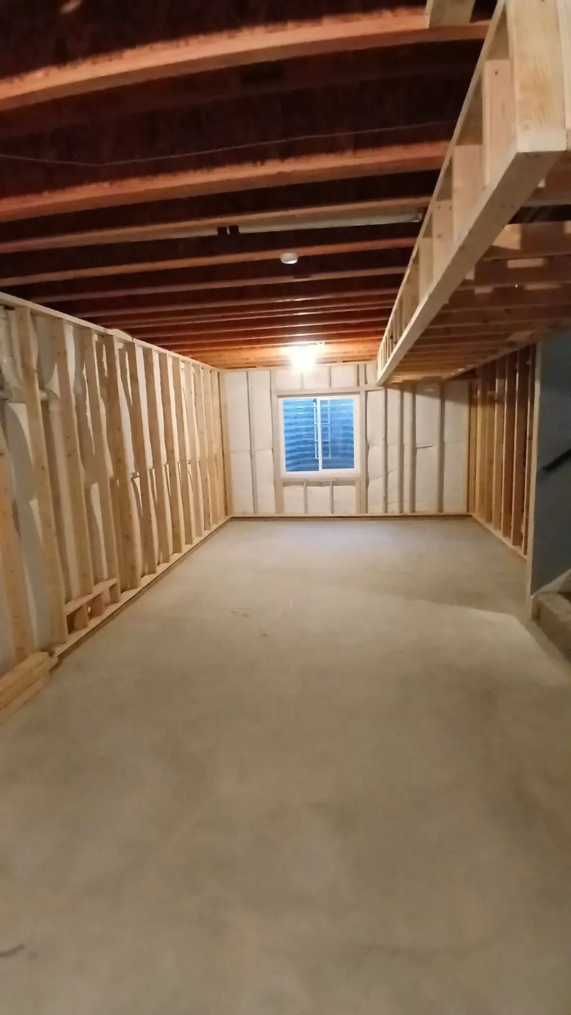 Unfinished basement with concrete floor, wood-framed walls and ceiling. A small window is in the back wall.