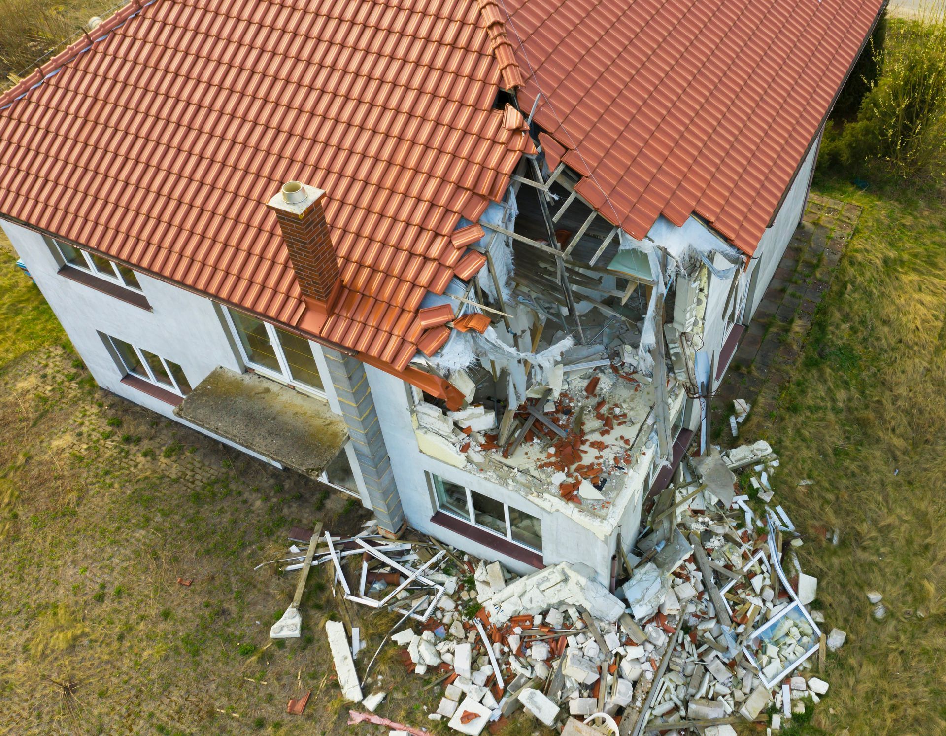 House with a large section of the exterior and roof destroyed, debris scattered on the ground.