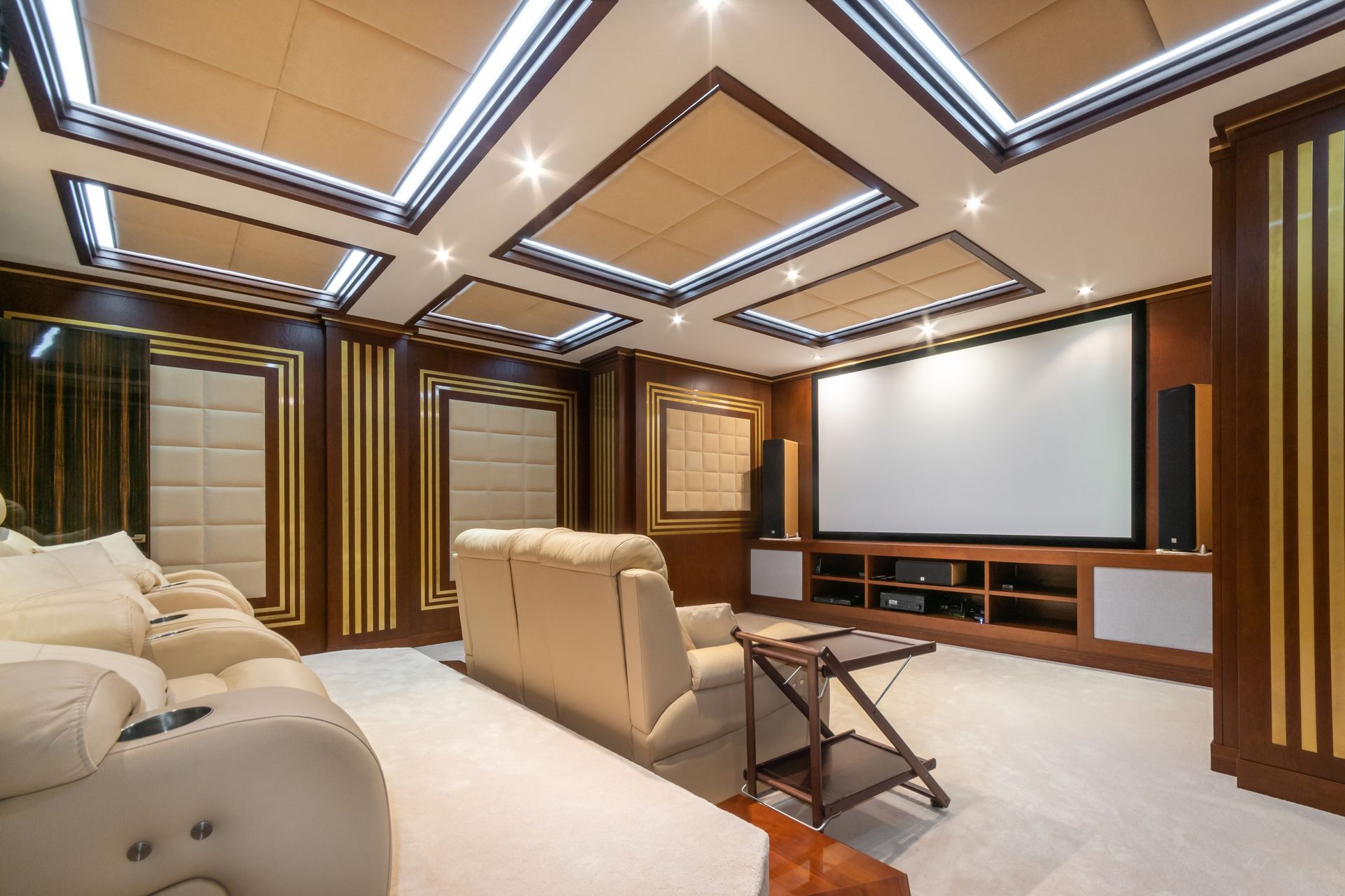 A luxurious home theater with cream-colored reclining chairs, dark wood accents, and a large projection screen.