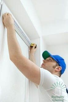 Burnaby Windows Contractor wearing a blue hat and white shirt measuring a residential window with a tape measurer.