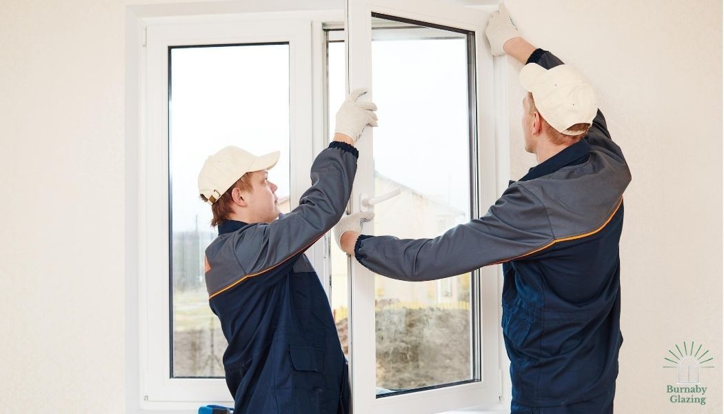 Burnaby Glazing contractors installing a new window on a new home. The window is a vinyl white frame and is being set in place by two workers wearing white gloves.