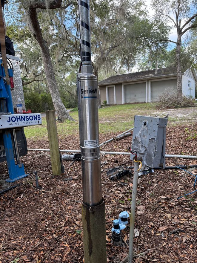 Well pump installed outdoors near a house with a damaged electrical box.
