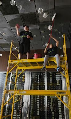 Two people are sitting on a yellow scaffolding cleaning the ceiling.