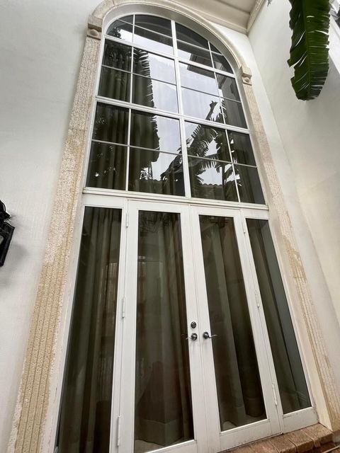 A tall, arched multi-pane window with white frames and light-blocking curtains, set into a light-colored stucco wall.