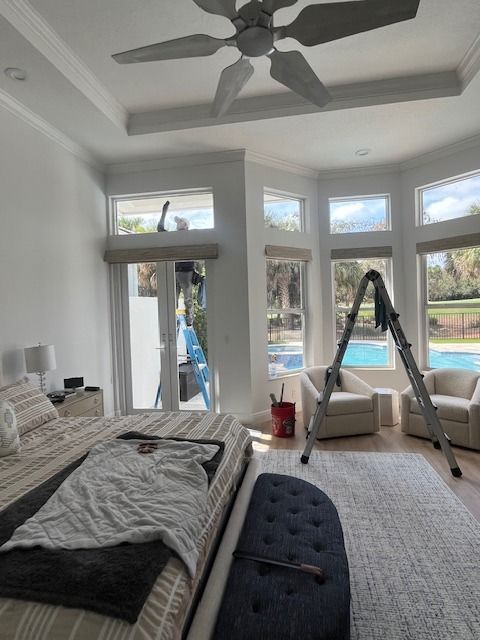 A bedroom featuring a bed, chairs, and a ladder placed near windows with a view of a pool area.