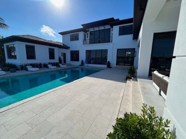 Modern white villa with a pool, large patio, and dark-framed windows under a bright blue sky.