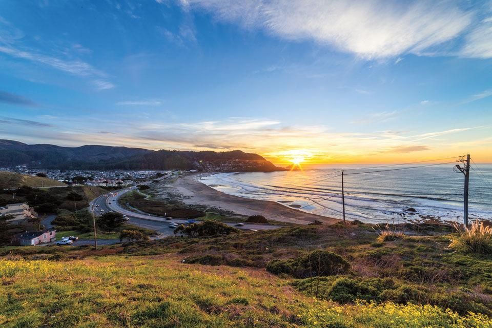 A view of a beach at sunset from a hill.