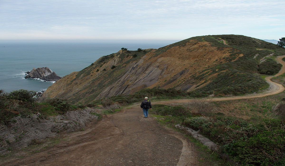A man is walking down a dirt road towards the ocean.