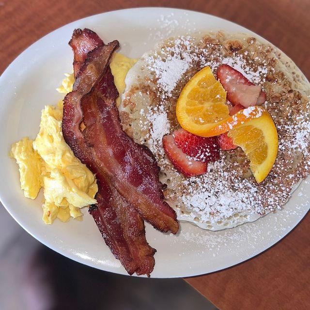 A plate of food with bacon eggs and fruit on it