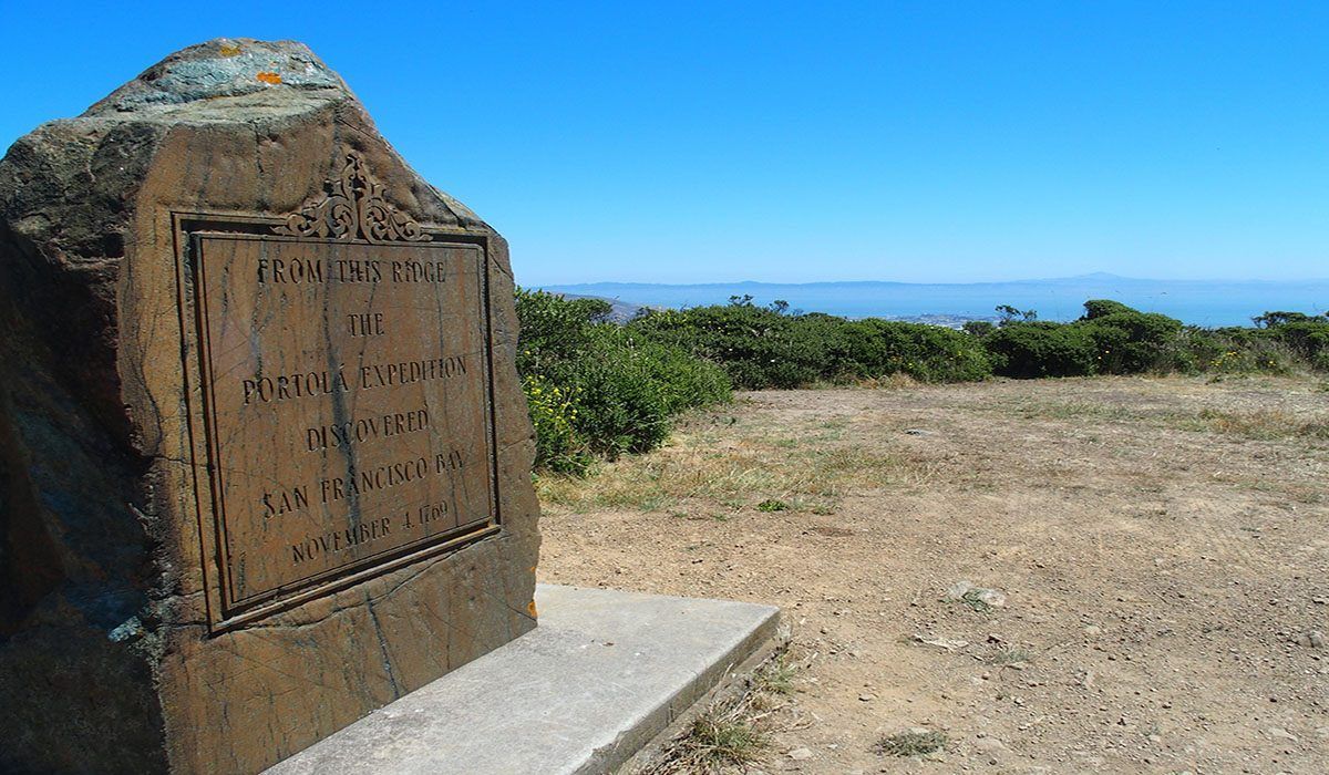 A large stone with a plaque on it is sitting in the middle of a dirt field.