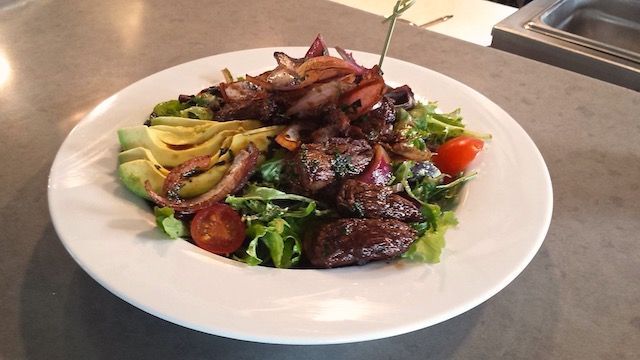 A white plate topped with a salad of meat and vegetables