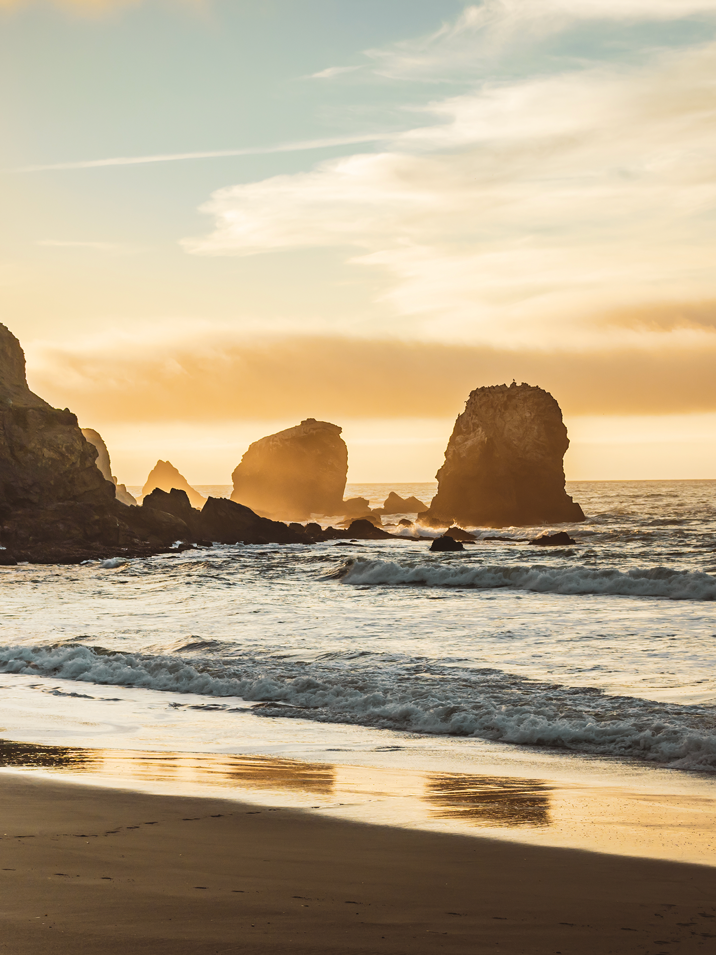 A beach with rocks in the water and a sunset in the background