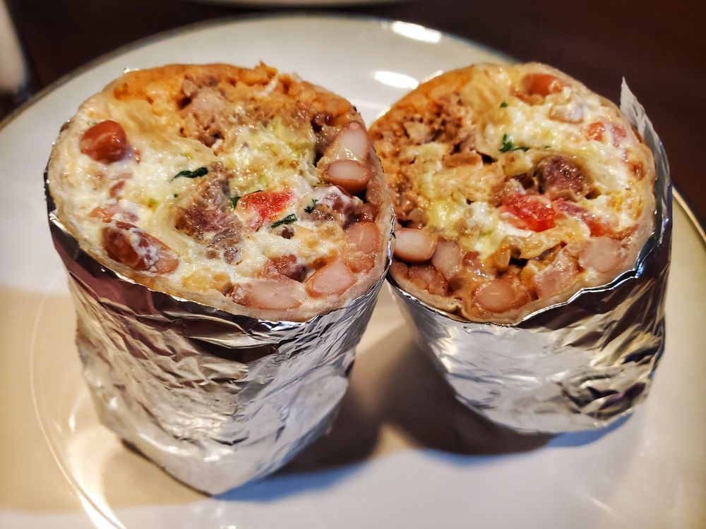 Two burritos wrapped in tin foil on a white plate