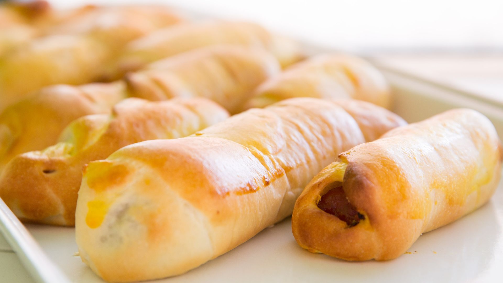 A bunch of hot dogs wrapped in bread on a white plate.
