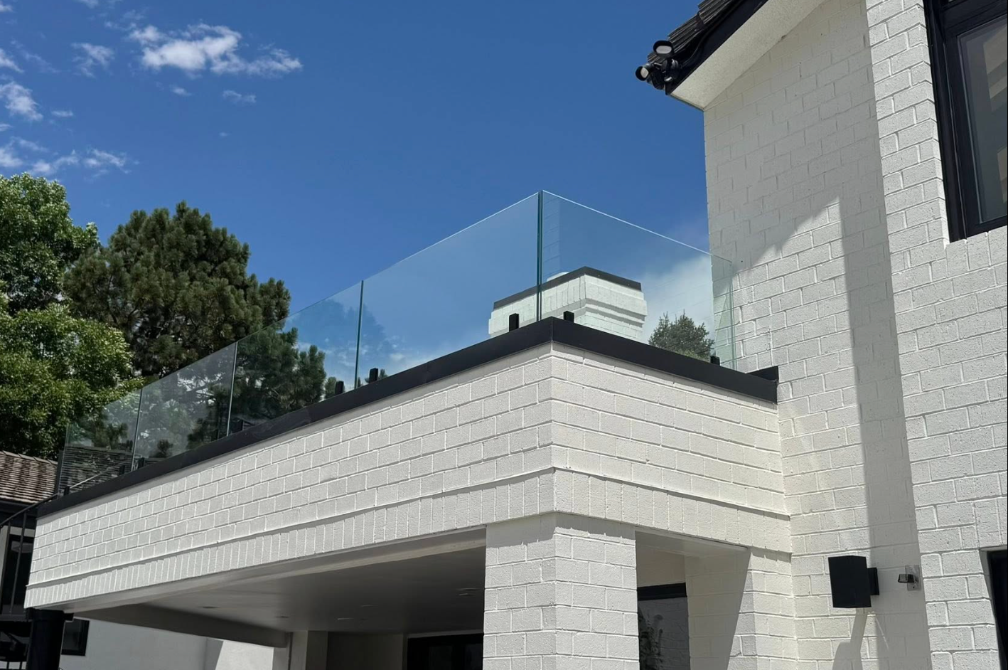 White brick building with glass balcony railing under a blue sky.