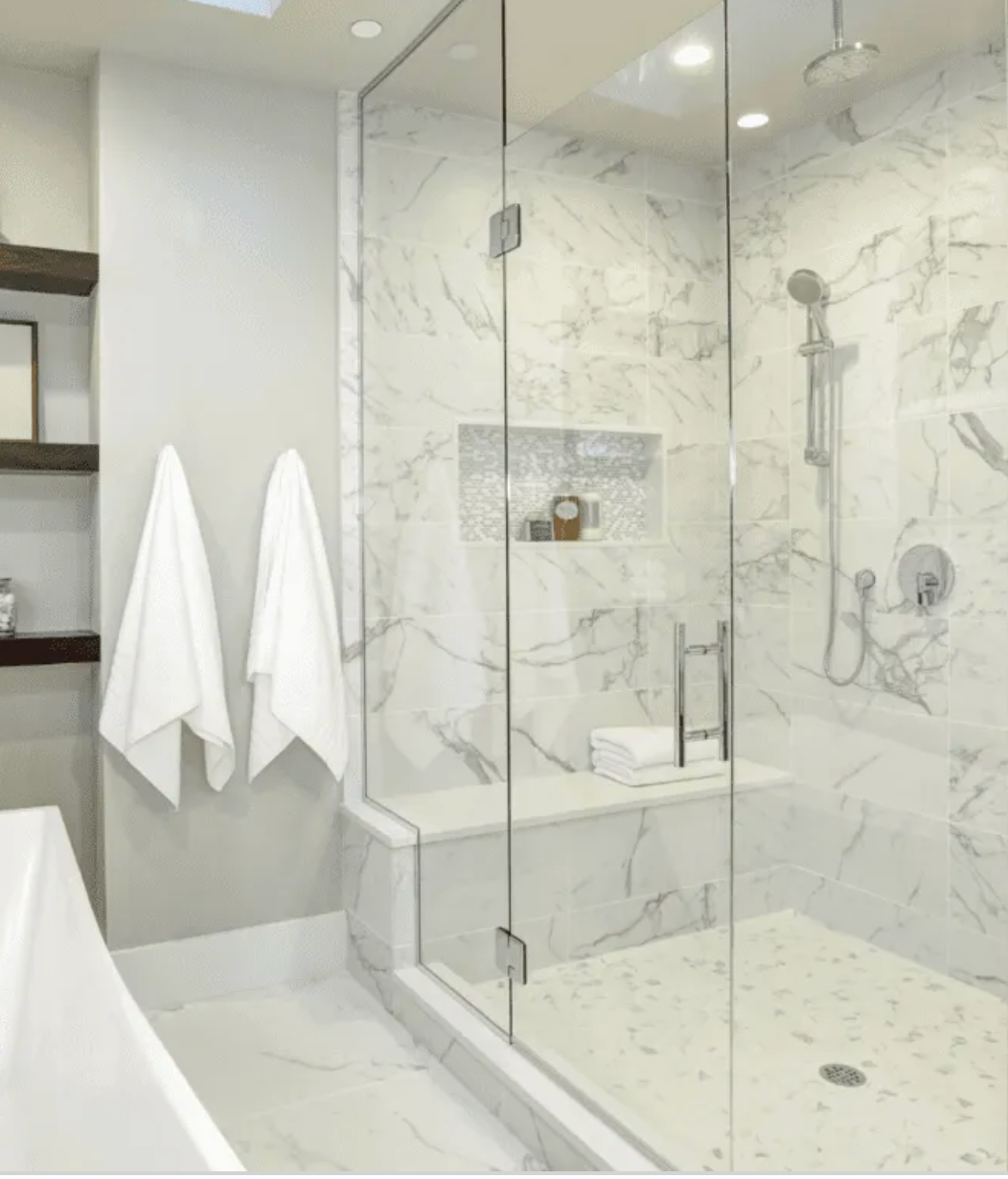 Bathroom with marble walls and glass shower, white towels hanging.