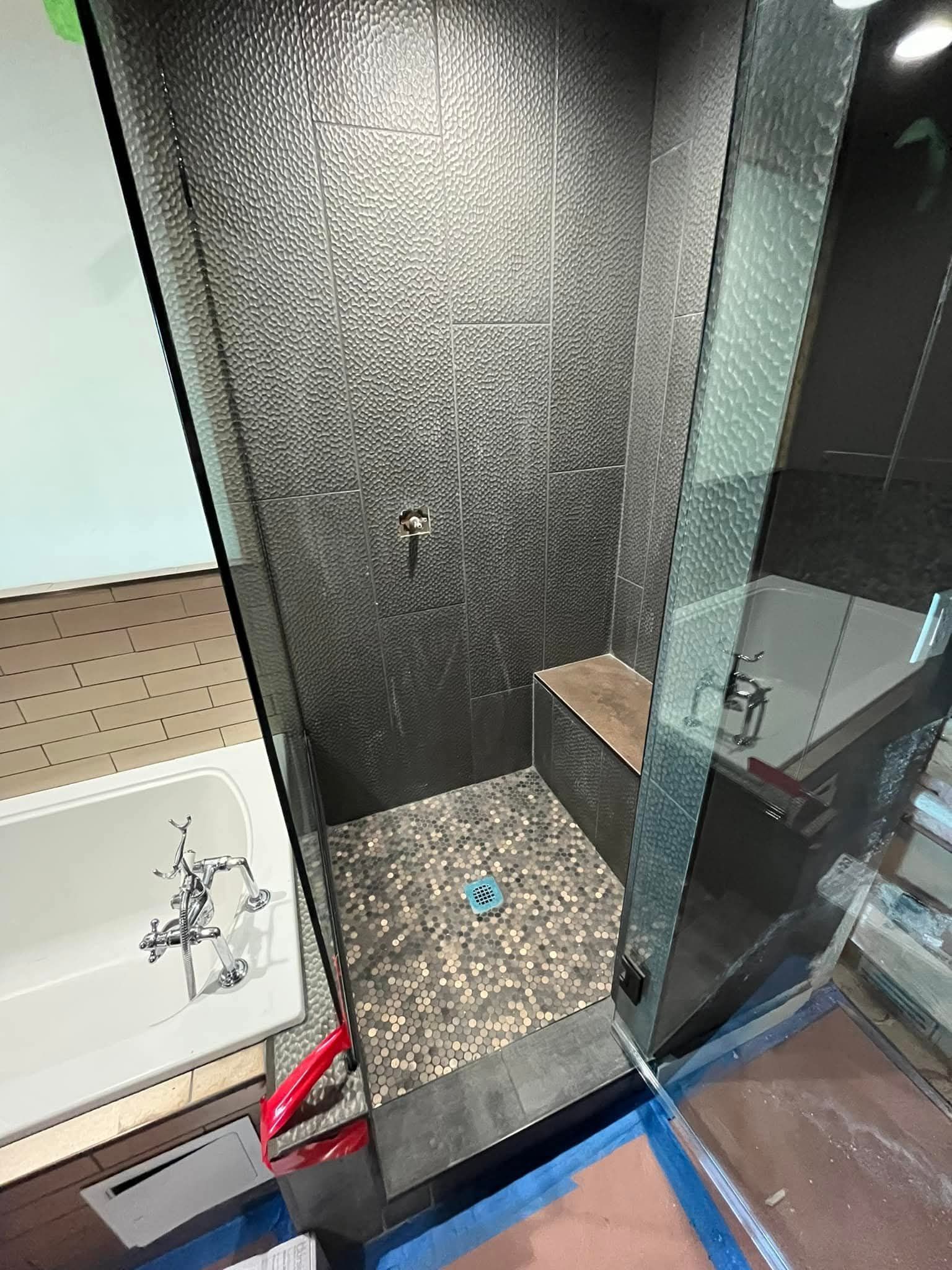 Small, modern shower with dark pebble floor, dark tiled walls, glass door, and bench.