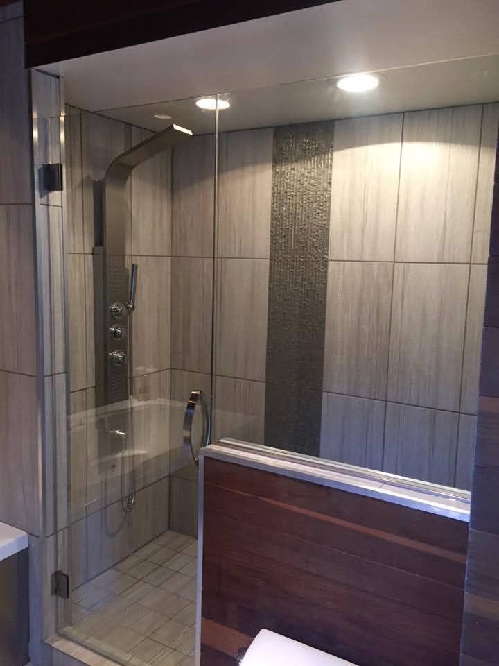 Modern shower with glass door, stainless steel fixtures, and wood accents; tiled walls.