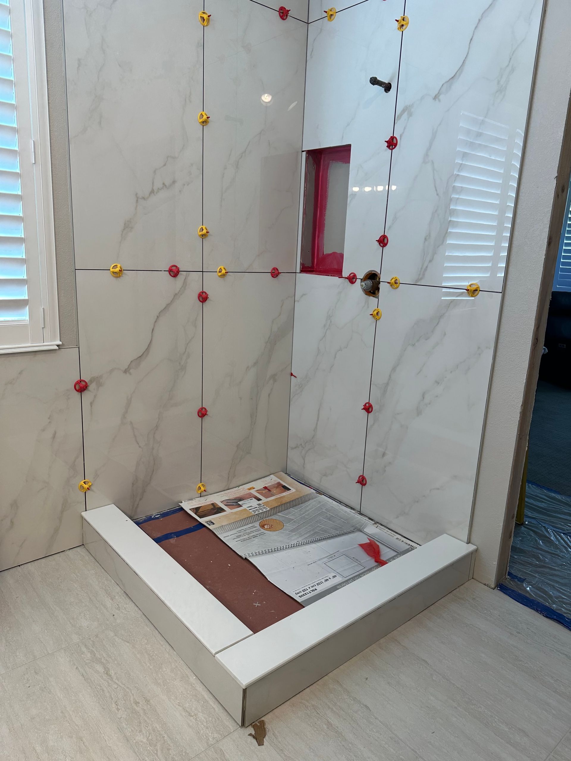 A tiled shower in progress, with leveling clips, marble-like tiles, and a small recessed shelf.