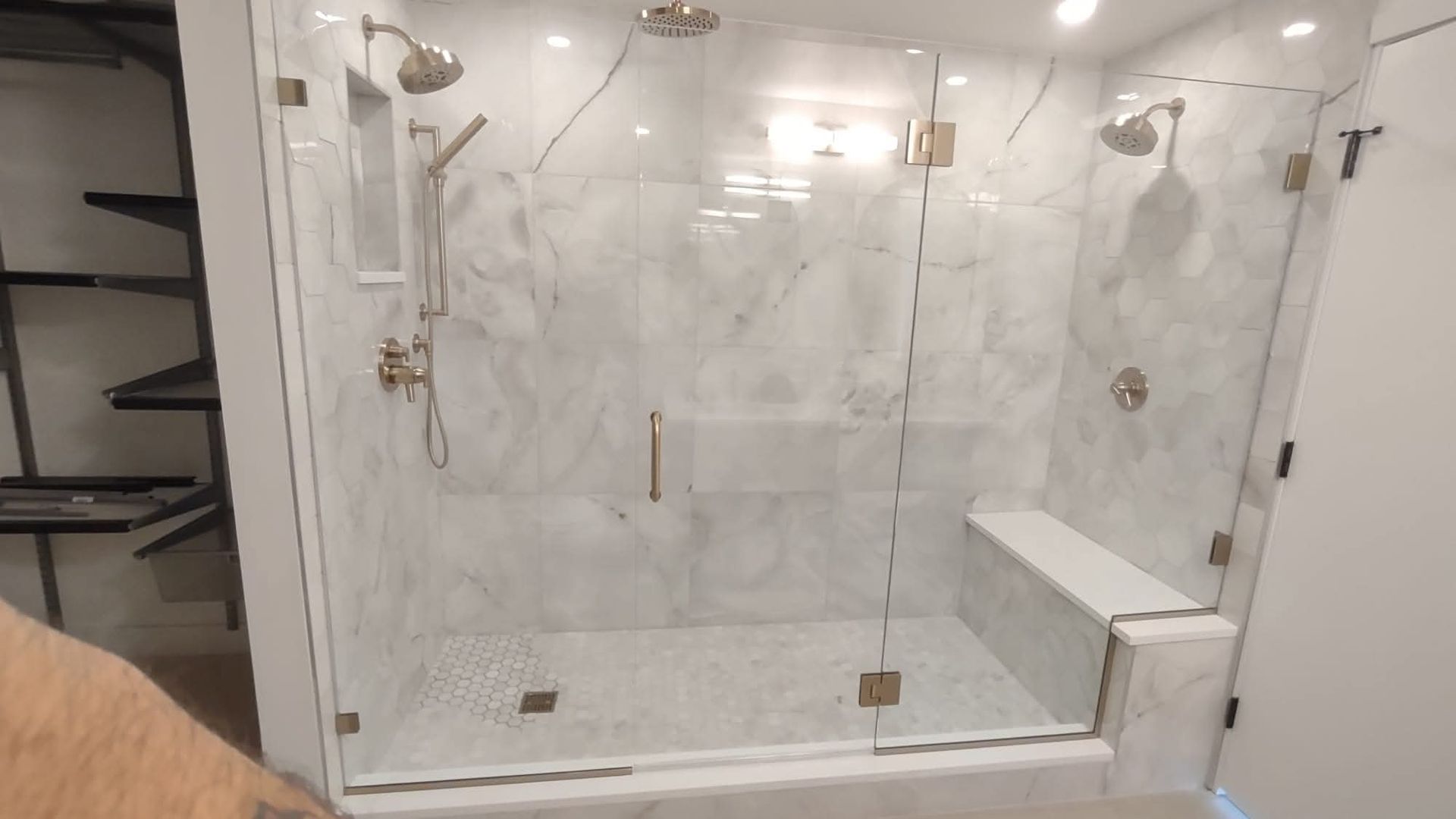 A luxurious white marble tiled shower with glass doors and gold fixtures.