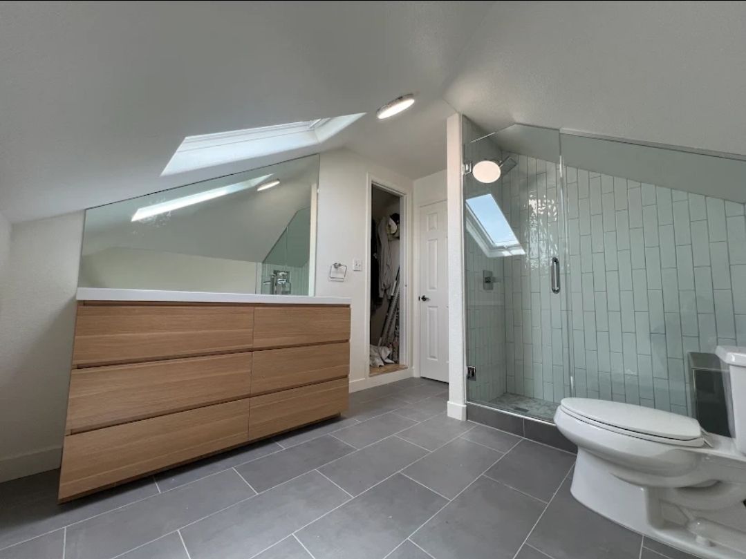 Bathroom with light wood vanity, gray tile floor, glass shower, and skylights.
