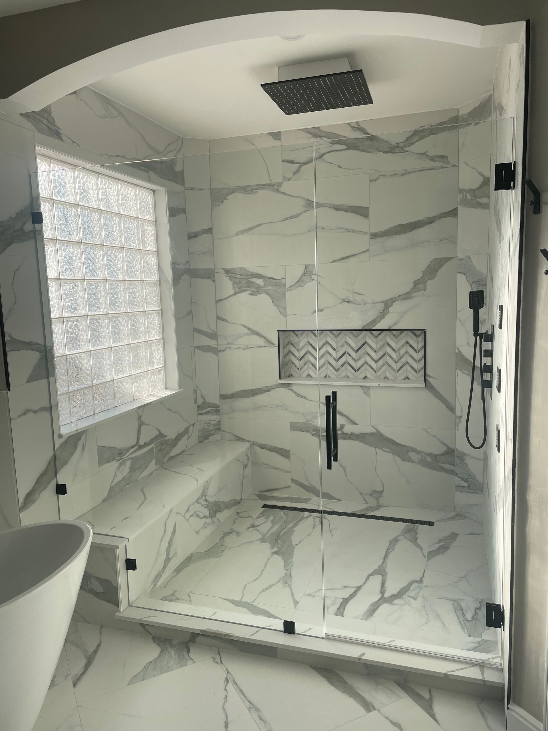 Modern marble-tiled walk-in shower with glass-block window, built-in shelf, and rainfall showerhead