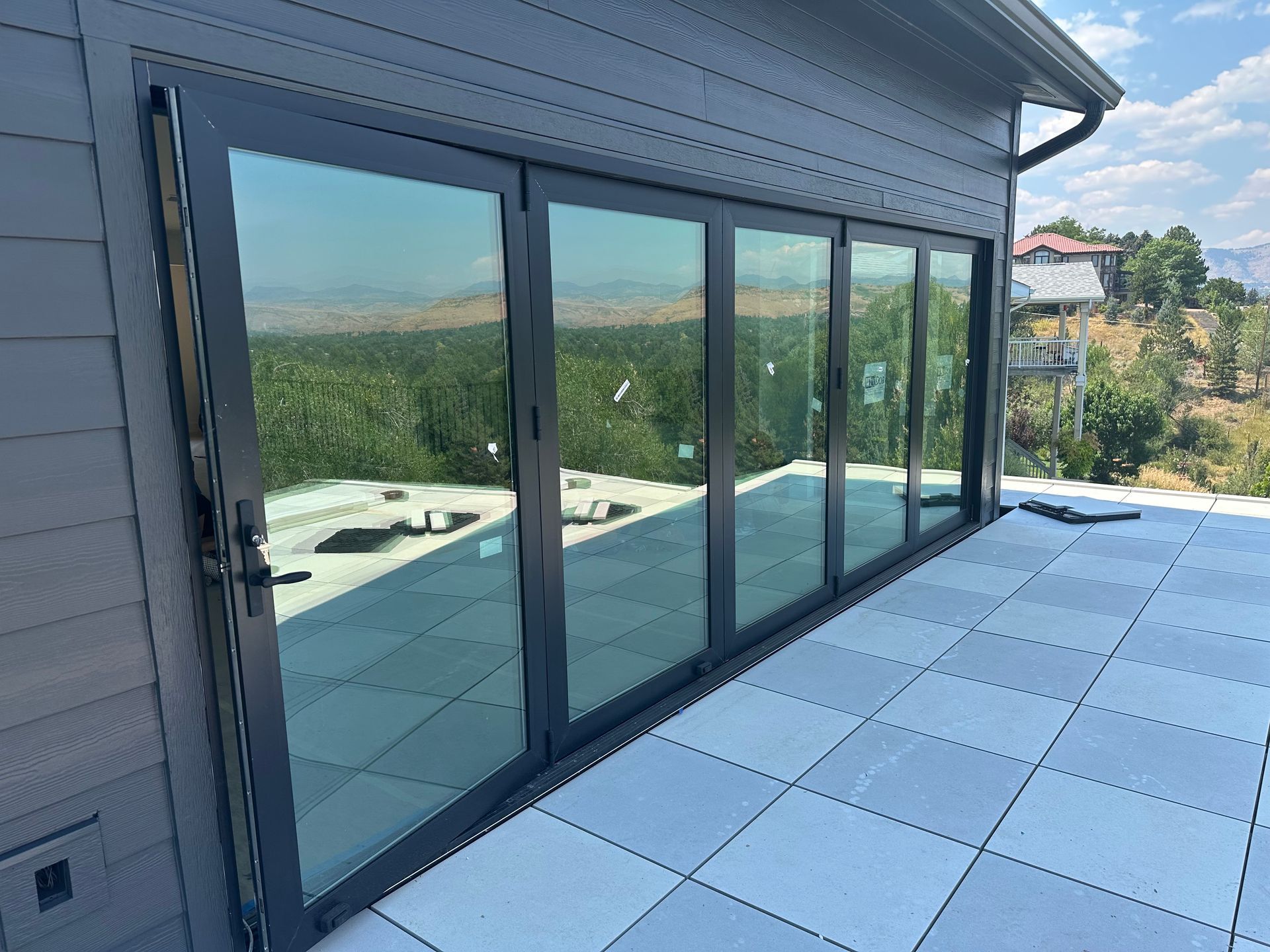 Exterior view of modern house with gray siding and large glass folding doors, overlooking landscape.
