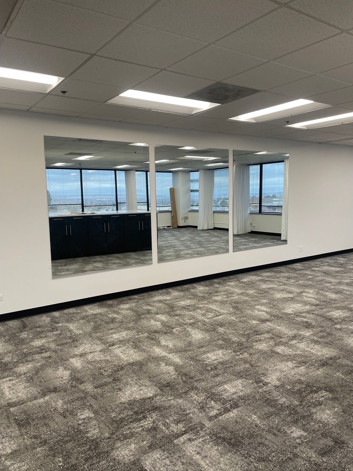 Empty office space with three large mirrors reflecting windows and carpeted floor.