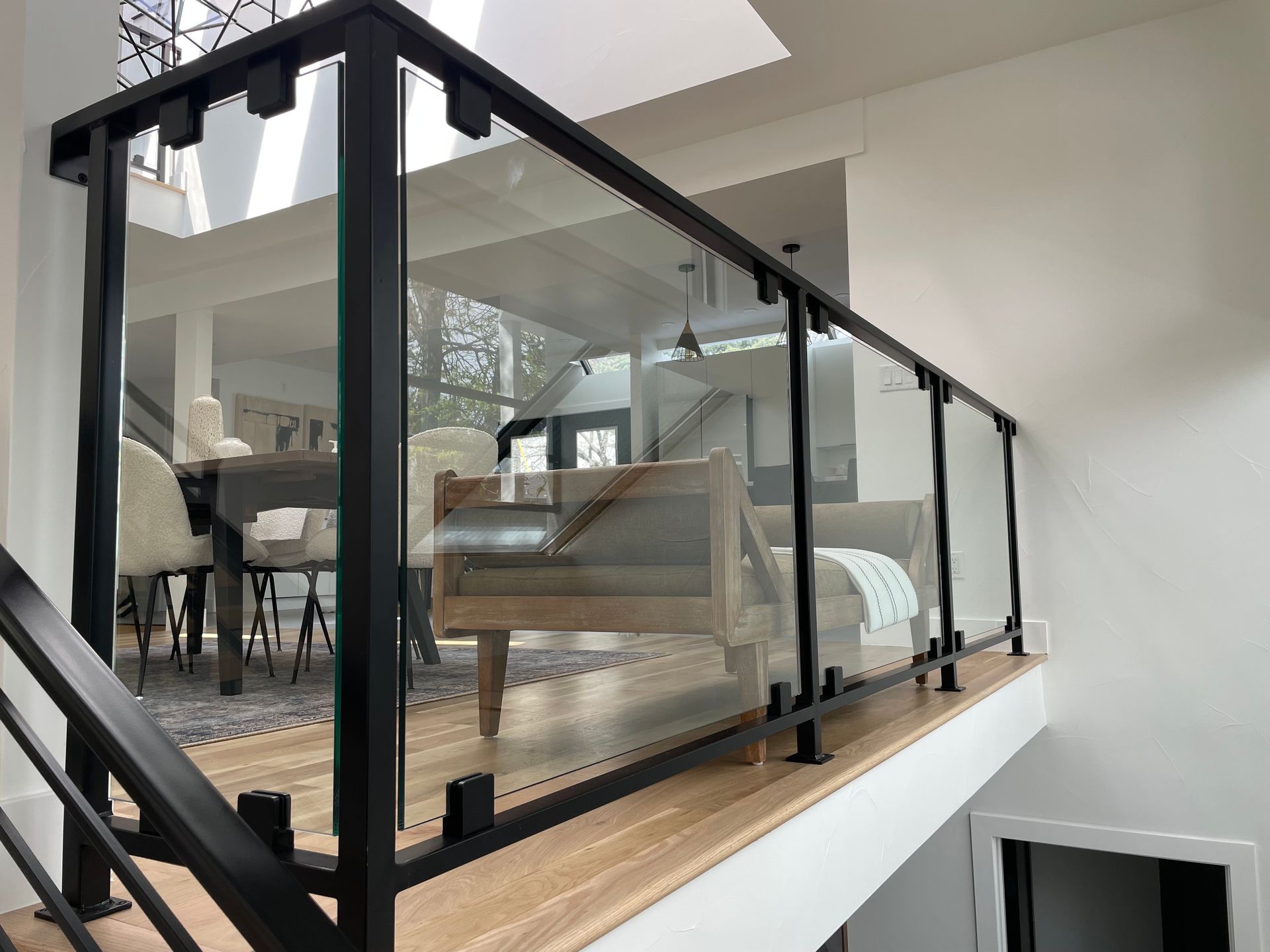 Black metal and glass railing on a second-floor walkway, overlooking a dining area with wood floors.
