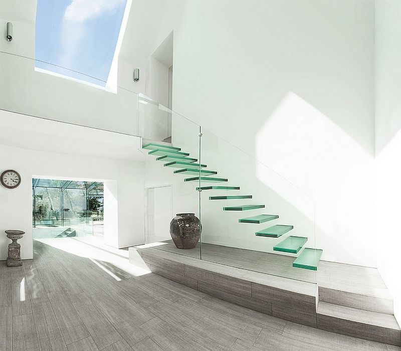 Modern white interior with floating glass stairs, natural light, and a decorative vase.
