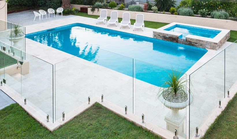 Swimming pool with glass fence, hot tub, lounge chairs, and manicured lawn.