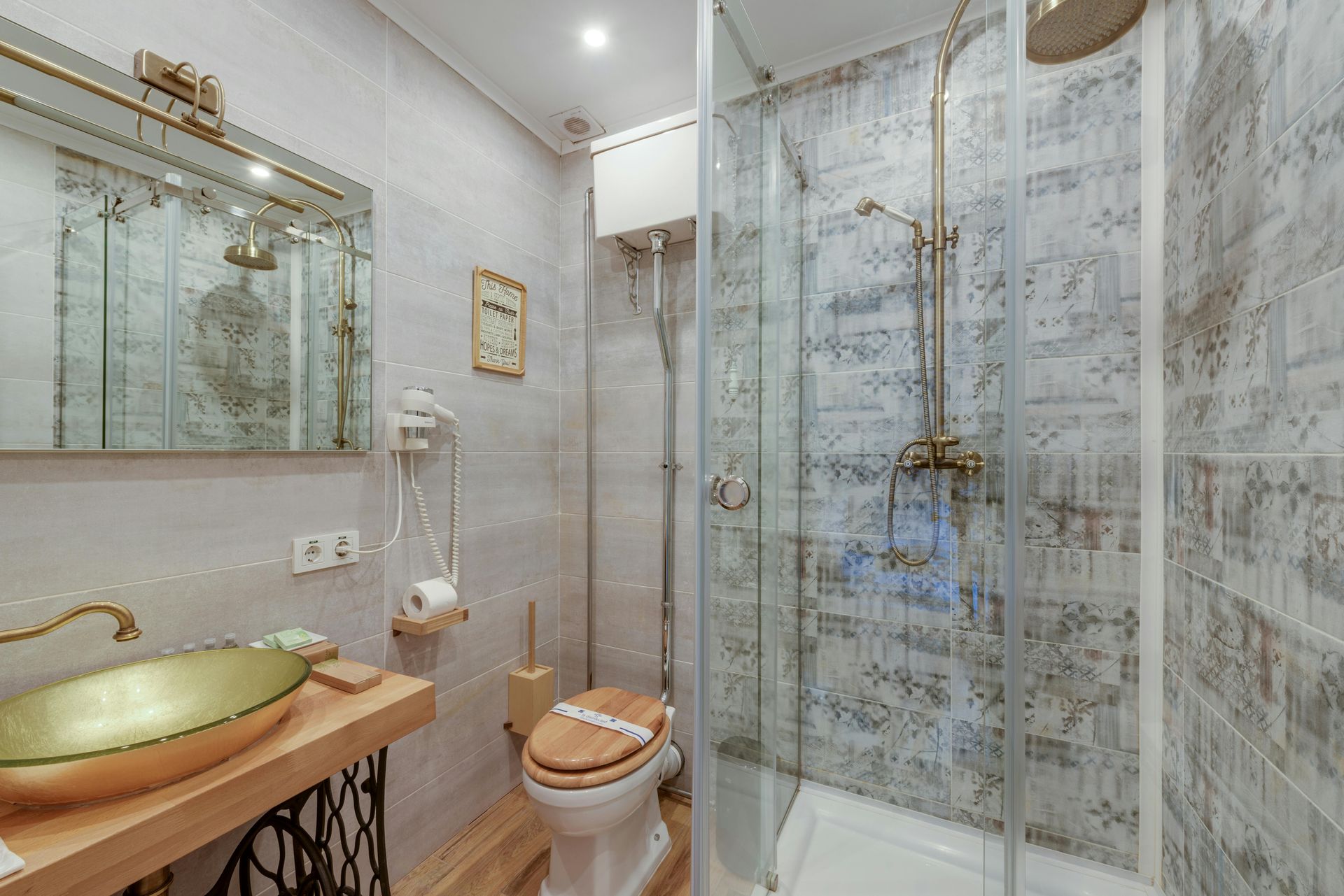 Bathroom with a gold sink, glass shower, toilet, and patterned grey walls.