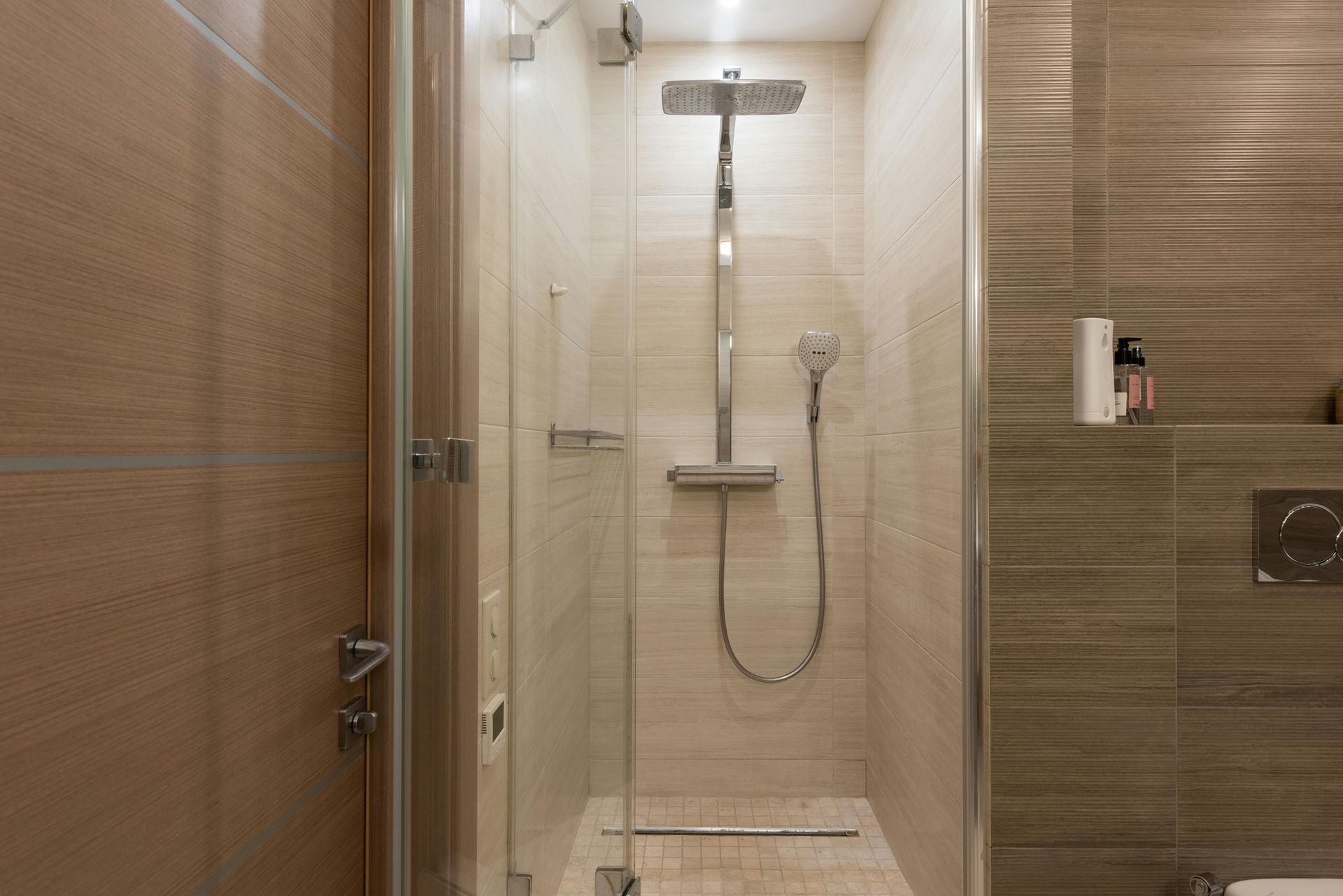 Shower stall with glass doors, chrome fixtures, and beige tile.
