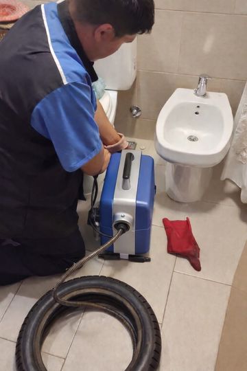 Técnico utilizando una máquina azul para desatascar desagües junto al lavabo del baño, con una manguera enrollada en el suelo
