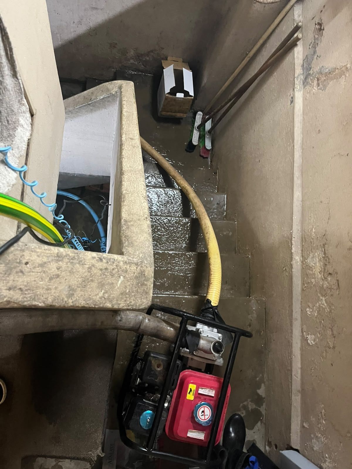 Pozo de servicio estrecho de hormigón, con tuberías, cables y un generador rojo en el fondo.