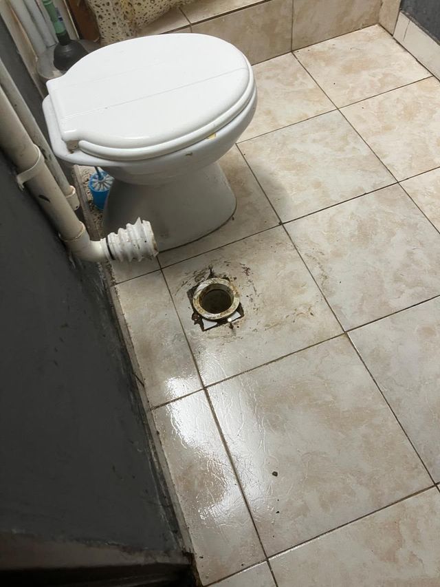 Baño pequeño con azulejos, un inodoro blanco y un desagüe de suelo a la vista a su lado.