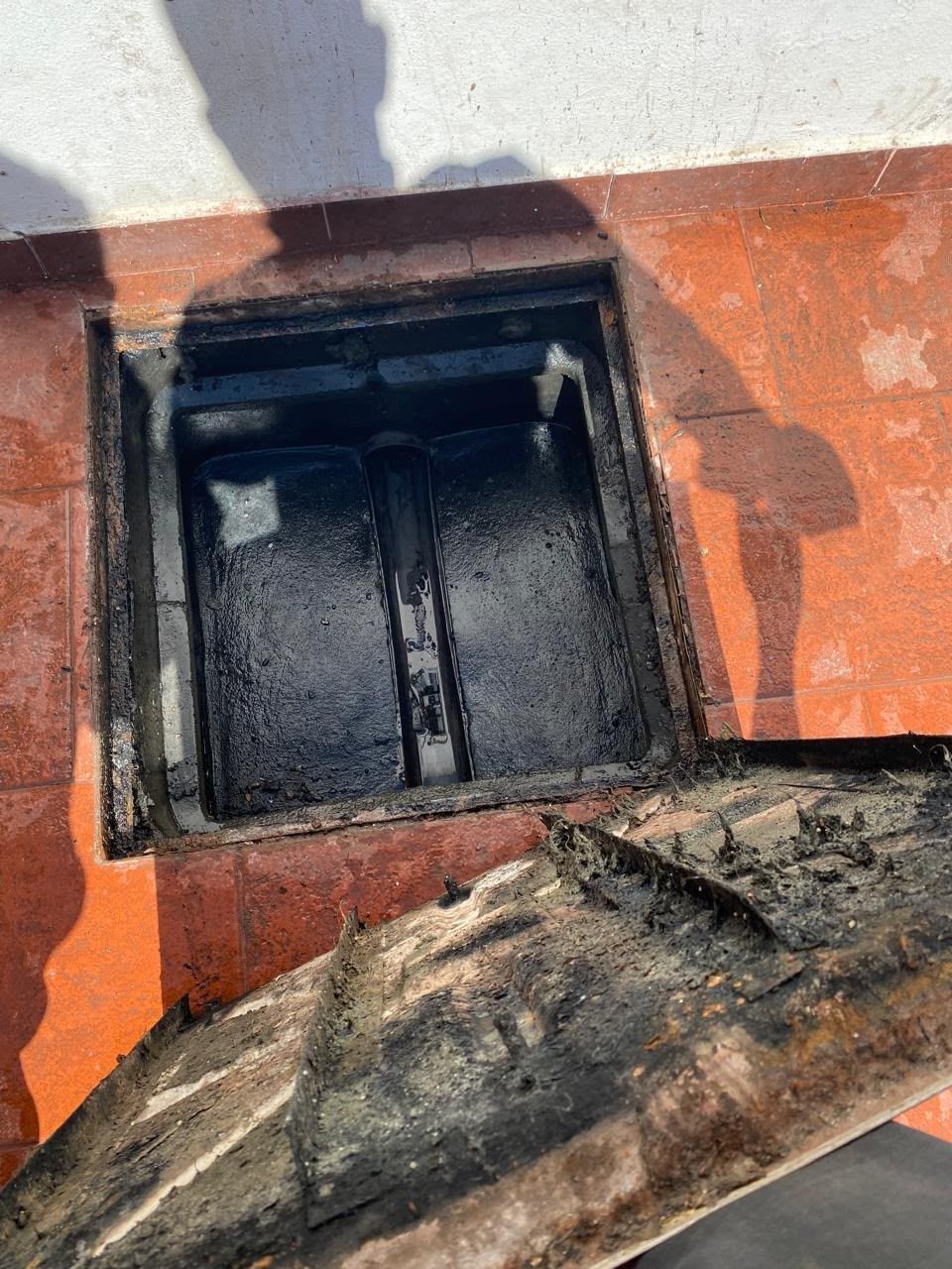 Escotilla de ventilación abierta en el tejado, con el interior negro y rodeada de una superficie pintada de naranja y blanco.